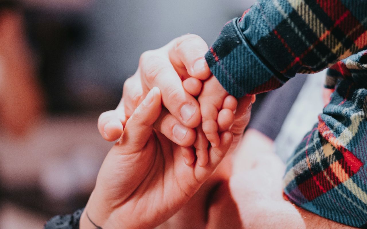Manos de un adulto sujetando la mano de un bebé